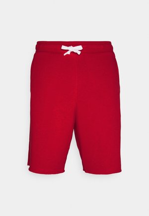 Røde shorts til knæet med en hvid snøre bundet i taljen på en ensfarvet lys baggrund.