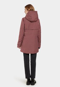 Roze parka met een capuchon, met een relaxte pasvorm en elastische manchetten, gecombineerd met zwarte broek en chunky zwarte laarzen.