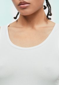 Biała bawełniana bluzka na ramiączkach z okrągłym dekoltem i cienkimi paskami, charakteryzująca się gładką fakturą i minimalistycznym wzornictwem.