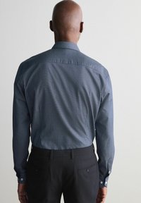 Camisa de manga larga de color azul oscuro con un pequeño patrón geométrico, cuello abotonado y textura suave, combinada con pantalones negros.