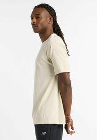Light beige short-sleeve t-shirt with a ribbed texture and crew neckline. Worn with dark pants featuring a logo on the leg.