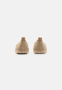 Beige canvas snörlösa skor med vävda jutesulor. Har en minimalistisk design och en liten dekorativ etikett bak.