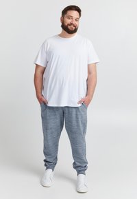 Wit katoenen T-shirt gecombineerd met grijze gemêleerde joggingbroek. De broek heeft een elastische tailleband en zijzakken. Witte sneakers maken de outfit compleet.