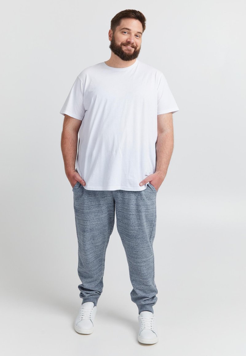 Wit katoenen T-shirt gecombineerd met grijze gemêleerde joggingbroek. De broek heeft een elastische tailleband en zijzakken. Witte sneakers maken de outfit compleet.