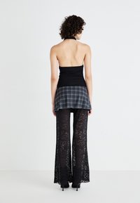 Μαύρο halter top, στρωμένο με γκρι καρό μίνι φούστα, συνδυασμένο με διάφανες μαύρες δαντελένιες παντελόνες σε φαρδιά γραμμή, δημιουργώντας μια εμφάνιση με ποικιλία υφών.