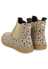 Botas de tobillo de ante beige con un patrón de estrellas negras, paneles laterales elásticos y puntera redonda; cuentan con botones de acento en tono dorado y suela texturizada.