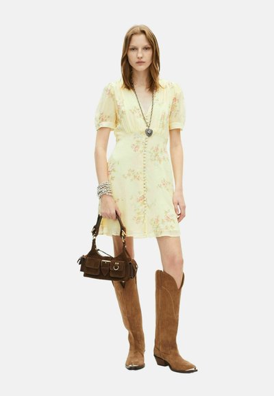Gul blomsterkjole med puffærmer og knapdetaljer, parret med brune ruskinds knælange støvler og en lille brun håndtaske.
