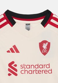 Cream Liverpool FC football jersey with red Adidas stripes on shoulders, red club crest, Adidas logo, and Standard Chartered sponsor text.