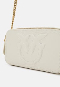 Cream leather bag with embossed logo design, featuring a gold-tone chain strap and zip closure. Smooth texture with contrast stitching details.
