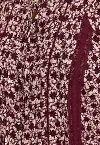 Tessuto a motivo floreale in bordeaux e crema, con pieghe, chiusure a bottone e dettagli in pizzo lungo i lati.