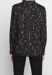 Maglietta nera a maniche lunghe con motivi colorati, che presentano cuori, stelle e forme geometriche. Tessuto morbido, colletto con bottoni e vestibilità ampia.