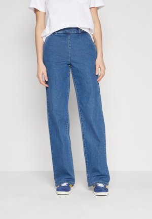 Løse blå denimjeans med høj talje. Har en glat tekstur og syninger langs sømmene. Båret med en almindelig hvid t-shirt.