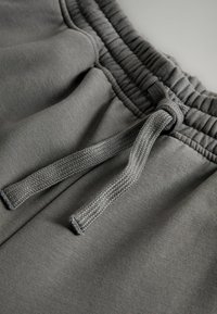 Graue Sweatpants mit einem elastischen Bund und einer sichtbaren Kordel. Der Stoff hat eine glatte Textur und minimale Nähedetails.