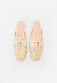 Scarpe slip-on in paglia tessuta color beige con una banda in pelle bianca, dettagli in oro e un accento con nappina sul davanti. Rivestimento interno liscio.