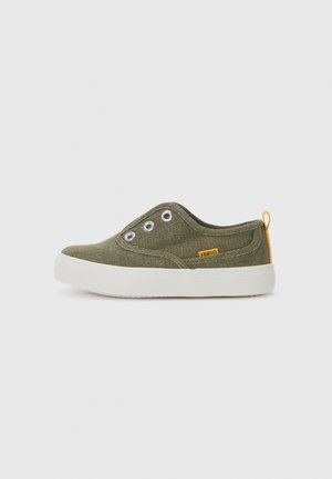 Chaussure en toile vert olive avec un bout rond, semelle en caoutchouc blanche et trois œillets en métal. Présente une étiquette d'accent jaune à l'arrière.