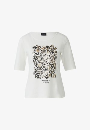 Biela tričko s krátkym rukávom s metalickým potlačením leopardieho vzoru v zlatej a čiernej farbe, s textom "STUDIO N°1 COLLECTION" pod grafikou.