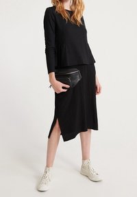 Musta pitkähihaine paita, jossa on kerätty vyötärö, yhdistettynä mustaan midi-hameeseen, jossa on sivureikä. Yhdistettynä valkoisiin korkeisiin tennareihin.