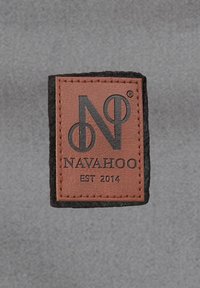 Bruine leren label met het reliëflogo "NAVAHOO" en "EST 2014" op een zwarte viltachtergrond; rechthoekige vorm met gestikte randen.