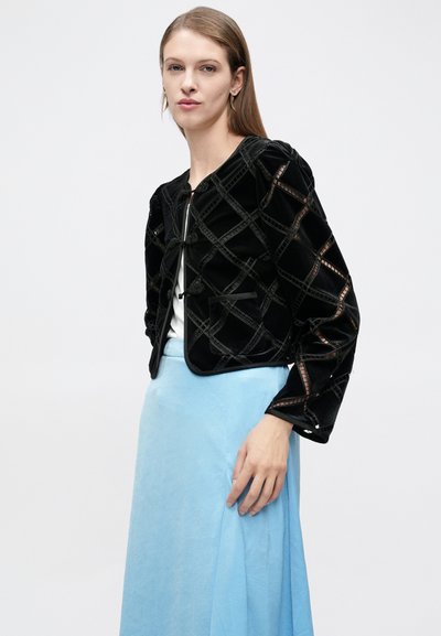 Μαύρο βελούδινο σακάκι με σχέδιο διαμαντένιου πλέγματος, διακοσμητικά κουμπιά και τσέπες με επιδιορθώσεις, συνδυασμένο με ανοιχτό μπλε φούστα.