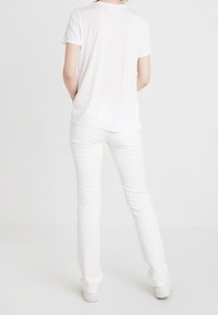 Camiseta blanca de manga corta y pantalones blancos ajustados. Tejido ligero y suave con un diseño sencillo, visto desde la parte de atrás.