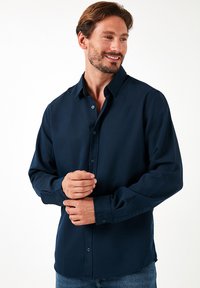 Camisa de manga larga azul marino con cuello extendido, frente abotonado y ajuste relajado. La tela tiene una textura suave y un ligero brillo.
