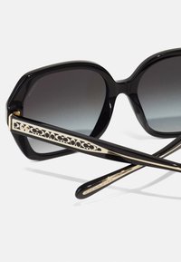 Ochelari de soare negri cu o ramă geometrică, lentile gri cu gradient și brațe accentuate cu aur, având un model decupat și detalii cu logo.