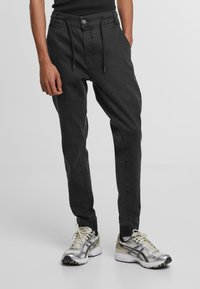 Čierne tapered jogger nohavice s pásom na šnúrku, bočnými vreckami a jemnými švovými detailmi, kombinované so striebornými a čiernymi športovými topánkami.