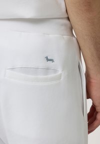 Pantalon blanc avec une finition texturée, présentant un petit logo de chien brodé bleu clair sur la poche arrière et deux poches arrière.