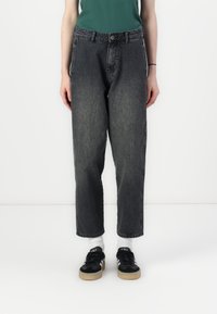 Černé džíny z denimu s volným střihem, se zapínáním na knoflík, poutky na opasek a bočními kapsami, doplněné černými teniskami.