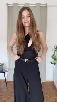Bodysuit negro sin mangas con un detalle de corte, combinado con unos pantalones de pierna ancha negros de cintura alta y un cinturón negro con una hebilla dorada.