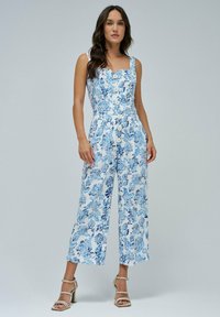 Mono floral en blanco y azul, con escote cuadrado, botones en el frente, piernas anchas y una tela ligera con un patrón texturizado.