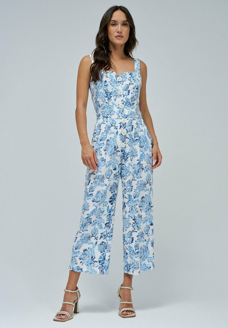 Mono floral en blanco y azul, con escote cuadrado, botones en el frente, piernas anchas y una tela ligera con un patrón texturizado.