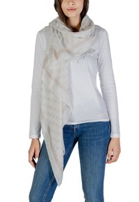 Sciarpa beige con design a fantasia e logo, in tessuto leggero, drappeggiata in modo morbido su una camicia bianca a maniche lunghe, caratterizzata da un accento argentato.
