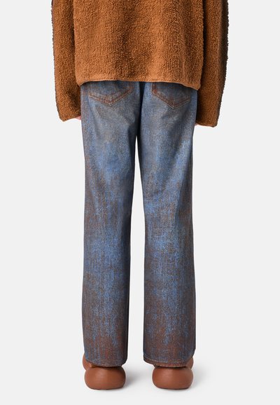 Maglione marrone peloso, jeans blu con texture e un leggero effetto usurato, e scarpe marroni rotonde, viste da dietro.