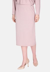  Lichtroze, knielange rok met een ribbeltextuur en een elastische tailleband. Gecombineerd met nude hoge hakken.