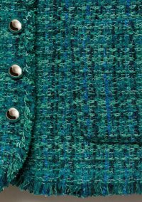 Tessuto tweed color turchese con una trama testurizzata, caratterizzato da bottoni metallici argentati e un bordo sfilacciato. Sono visibili varie sfumature di verde e blu.