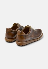 Zapatos de cuero marrón con un acabado suave, punta redondeada y cordones a juego. Presentan un reverso texturizado y una suela de goma con patrones circulares.