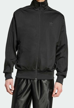 Giacca sportiva nera con colletto alto, zip completa e tre strisce verticali sulle maniche. Tessuto liscio e leggero.