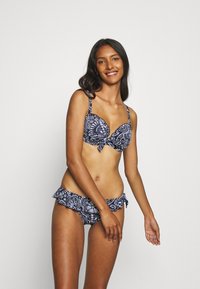 Biquíni azul-marinho com padrão floral branco; parte de cima com acolchoamento e detalhe de laço, alças ajustáveis e bordas inferiores franzidas.
