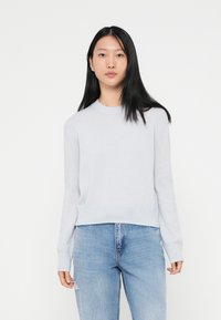 Ljust grått stickat tröja med rund halsringning, långa ärmar och ribbade manschetter, parat med blå slitna jeans.