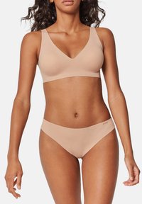 Beżowy bezprzewodowy biustonosz i dopasowane majtki bikini, minimalistyczny design, gładka tekstura, miękka tkanina, kształt v-neck, brak widocznych elementów metalowych lub wzorów.
