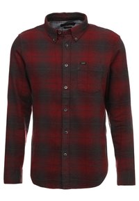 Camicia in flanella a quadri rossi e grigi con maniche lunghe, chiusura con bottoni e taschino sul petto. Presenta un piccolo etichetta del marchio sul petto.