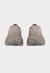 Paire de baskets beiges épaisses vues de dos avec des semelles épaisses comportant des coussinets circulaires et des accents verts subtils.