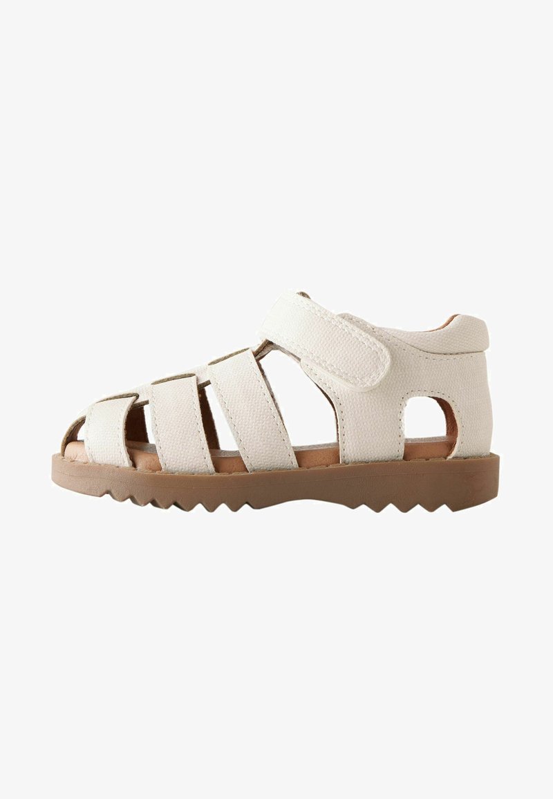 White sandal made of textured material with multiple cutouts, Velcro strap, and a rugged tan rubber sole. Offers a secure fit.