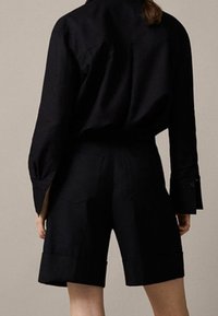 Svart skjorta med knappar, långa ärmar och sidslitsar, kombinerad med skräddarsydda svarta shorts med platta fickor och rak benform.