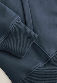 Gros plan d'un sweat-shirt bleu marine montrant le poignet et la ceinture côtelés avec des coutures visibles et une texture de tissu coton doux.