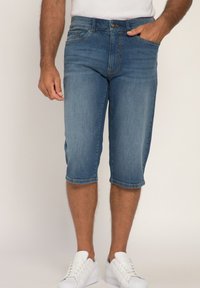 Denim bermuda shorts i en lys blå vask, med fem lommer, knaplukning og afsluttet med stikninger i kanten. Møder hvide sneakers.