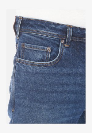 Granatowe dżinsy o klasycznym designie pięciu kieszeni, z miedzianymi nitami, pomarańczowymi przeszyciami i gładką teksturą.