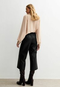 Blusa beige fluida con mangas abullonadas, combinada con culottes de imitación cuero negro de cintura alta. Botas de tacón marrones completan el look.