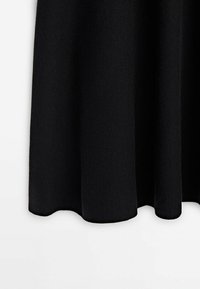 Jupe en tissu noir avec une texture douce suspendue droite, présentée sur un fond blanc avec des bords d'ourlet légèrement festonnés.